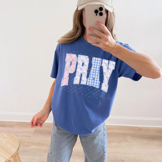 Person wearing a blue t-shirt with 'PRAY' printed on it, taking a mirror selfie.