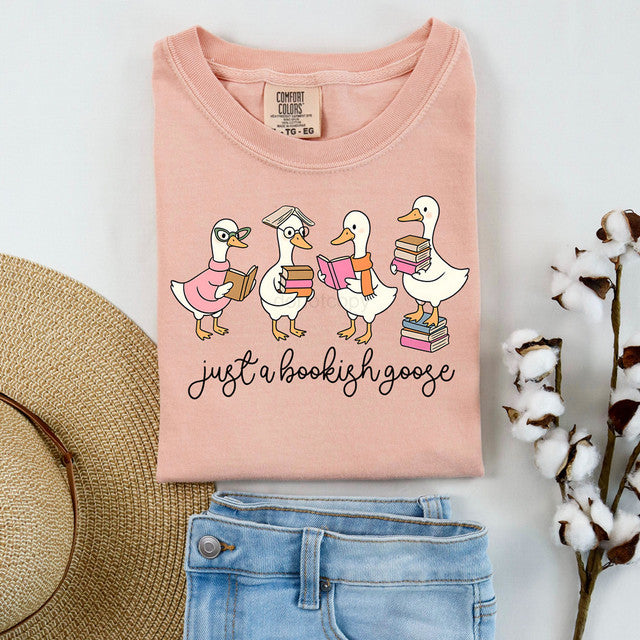 Pink t-shirt with cartoon ducks and 'just a bookish goose' text, displayed with jeans and a hat.