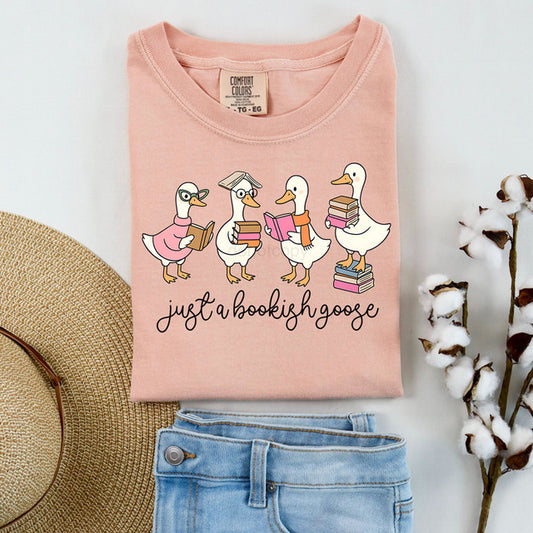 Pink t-shirt with cartoon ducks and 'just a bookish goose' text, displayed with jeans and a hat.