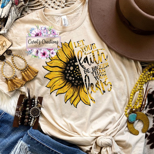 Beige t-shirt with sunflower design and text, surrounded by accessories on a textured surface.
