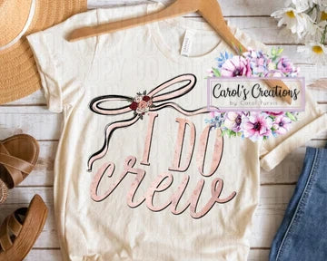 Beige t-shirt with 'I Do Crew' text and floral design on a wooden surface.