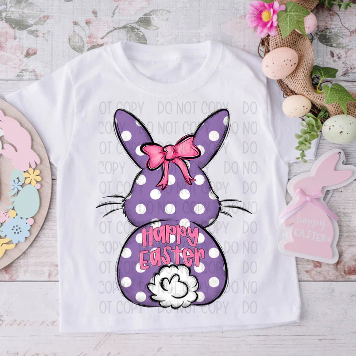 White t-shirt with a purple polka dot bunny design and 'Happy Easter' text, surrounded by Easter decorations.
