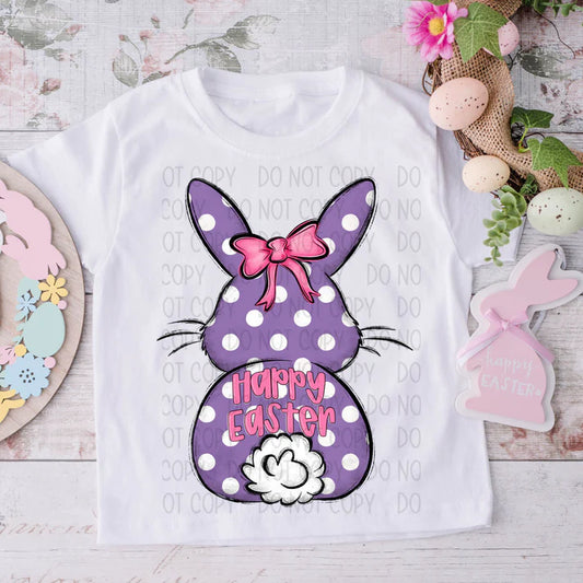 White t-shirt with a purple polka dot bunny design and 'Happy Easter' text, surrounded by Easter decorations.