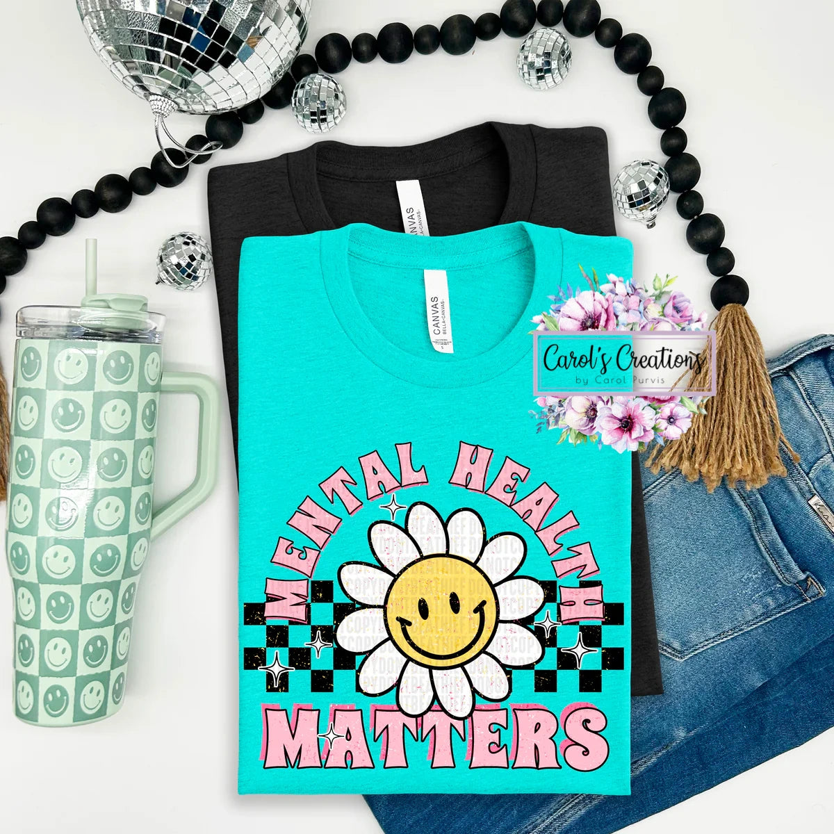 Turquoise t-shirt with 'Mental Health Matters' design, green tumbler, disco ball, and denim jacket on a white background