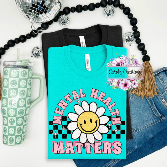 Turquoise t-shirt with 'Mental Health Matters' design, green tumbler, disco ball, and denim jacket on a white background