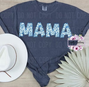 Navy blue t-shirt with 'MAMA' text, white hat, and floral decorations on a light wooden surface.