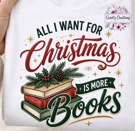 A white graphic t-shirt held by a hand, featuring a festive Christmas design with the text 'ALL I WANT FOR Christmas IS MORE Books' in red and green lettering, decorated with an illustration of stacked books, holly, and pinecones. A 'Carol's Creations' brand logo is visible in the top right corner.
