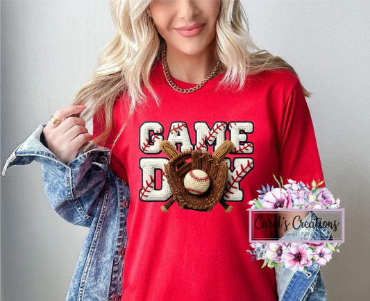 Person wearing a red t-shirt with 'Game Day' and sports-themed graphics, holding a denim jacket and flowers.