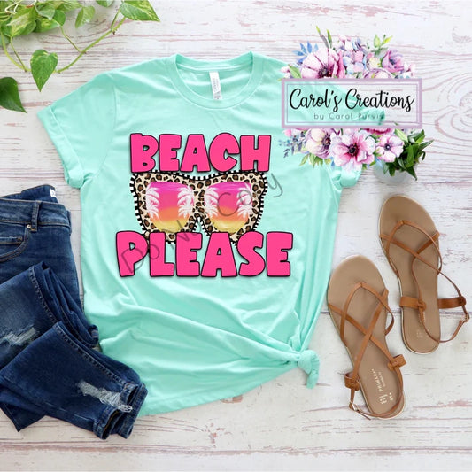 Mint green t-shirt with 'Beach Please' design, paired with denim shorts and sandals on a wooden surface.
