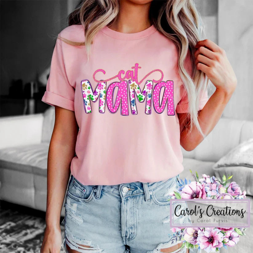 Person wearing a pink t-shirt with 'Cat Mama' text, standing in a living room.