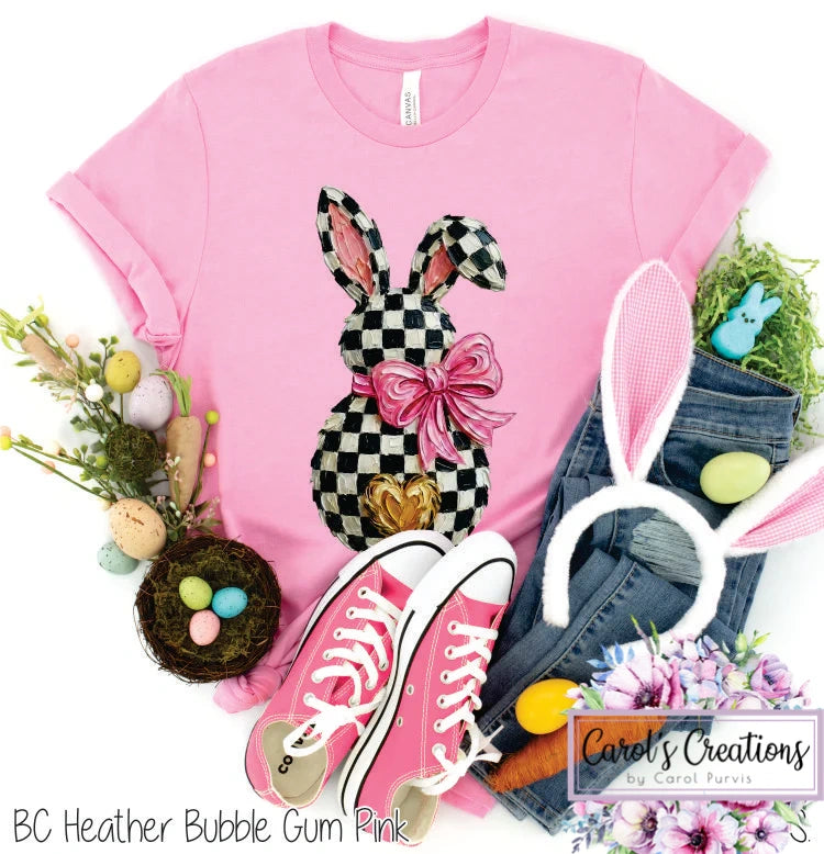 Pink t-shirt with checkered bunny design, pink sneakers, denim shorts, and Easter decorations on a white background.