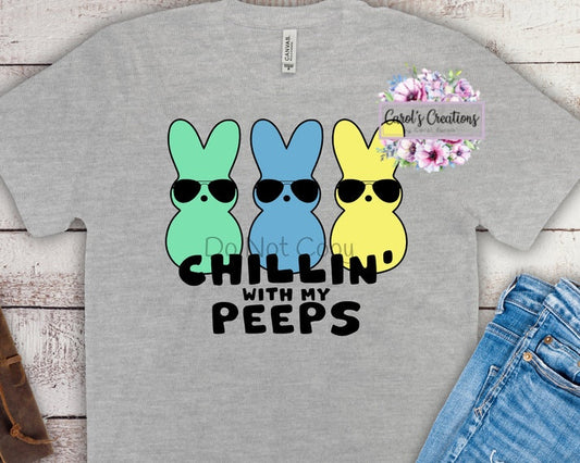 Gray t-shirt with colorful bunny design and text 'Chillin with my peeps' on a wooden surface.