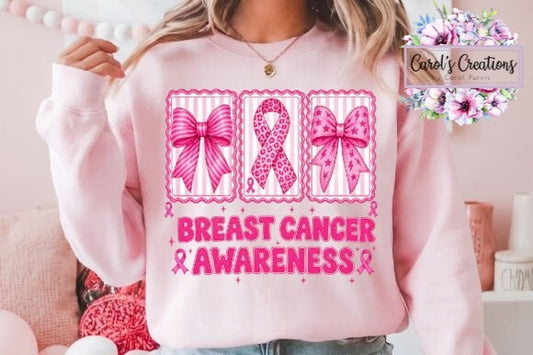 A person wearing a light pink sweatshirt with a breast cancer awareness graphic featuring three pink ribbon designs and the text 'BREAST CANCER AWARENESS' in pink. The photo is taken indoors with a soft pink room background, and a 'Carol's Creations' watermark appears in the top right.