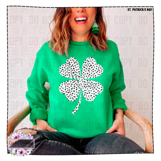 Person wearing a green sweater with a black and white shamrock design, sitting on a chair.