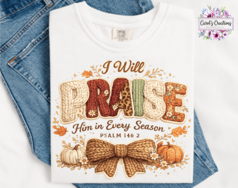 A folded white graphic T-shirt laid flat on top of blue jeans. The shirt features a large autumn-themed embroidered-style design with the words 'I Will Praise Him in Every Season' and 'PSALM 146:2,' plus pumpkins, leaves, and a bow motif.