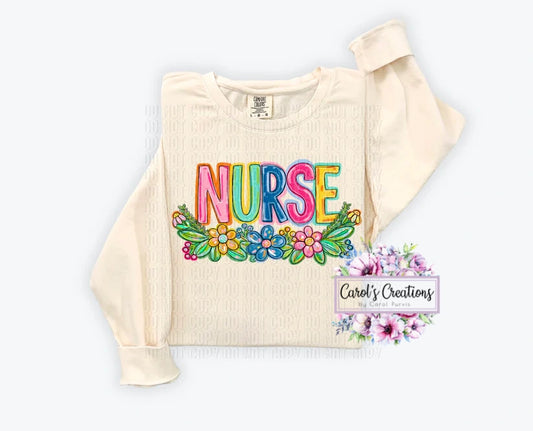 Beige cropped sweatshirt with 'NURSE' in colorful letters and floral designs on a white background.