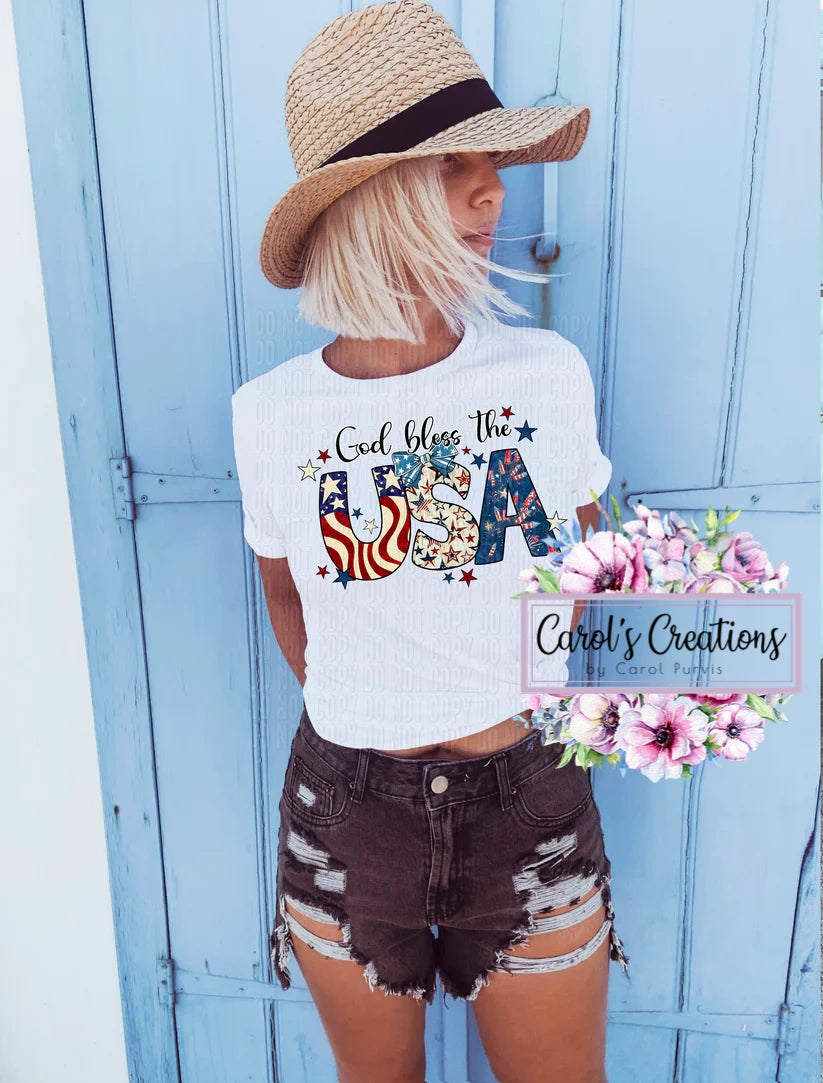 Woman wearing a white t-shirt with 'God bless the USA' design, standing in front of a blue wooden door.