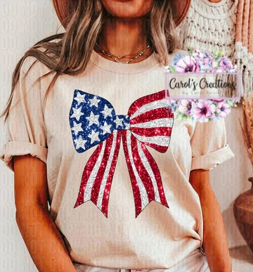 Person wearing a beige t-shirt with an American flag bow design, sitting indoors.