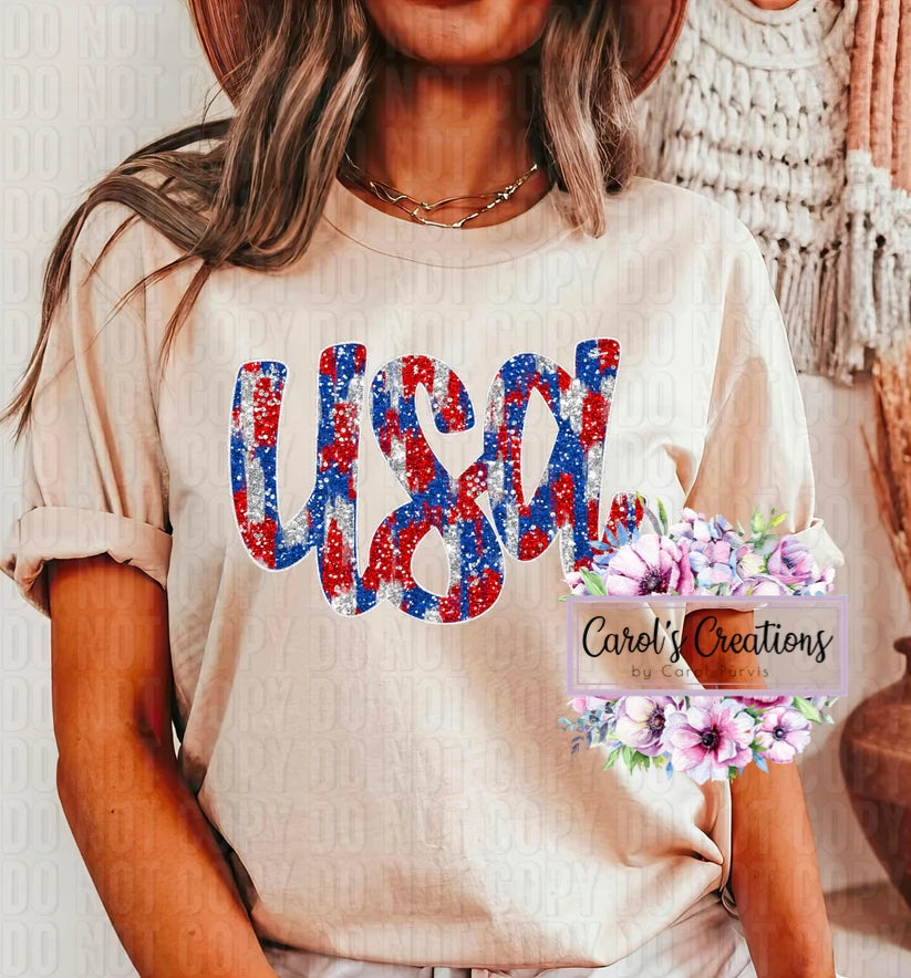 Person wearing a beige t-shirt with 'USA' in red, white, and blue, standing in front of a decorative wall.