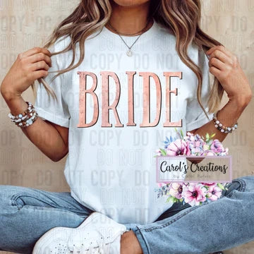 Woman wearing a white t-shirt with 'BRIDE' printed on it, sitting on a wooden floor.