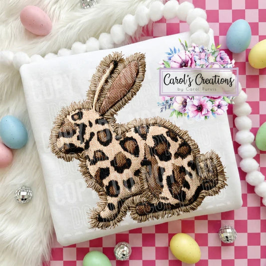 Leopard print bunny patch on a white fabric with 'Carol's Creations' branding, surrounded by Easter eggs and decorations.