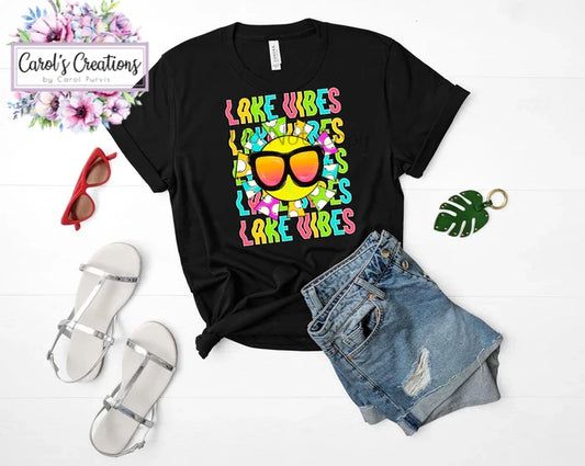 Black t-shirt with 'Lake Vibes' design, sunglasses, sandals, and shorts on a white background.
