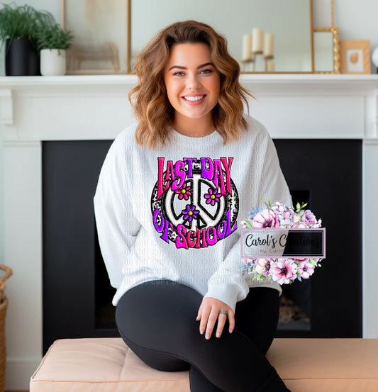 Woman wearing a white sweatshirt with 'Last Day of School' design, sitting in a room with a fireplace.