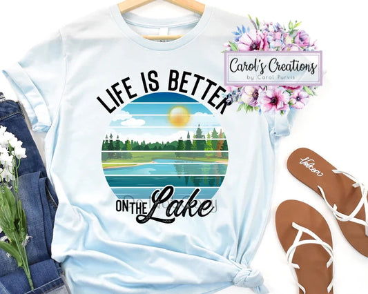 White t-shirt with 'Life is Better on the Lake' design, floral decorations, and 'Carol's Creations' branding.