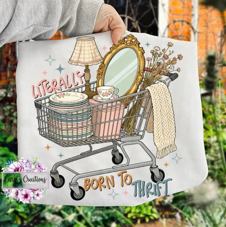 Tote bag with a shopping cart illustration and 'Born to Thrift' text, held against a blurred outdoor background.
