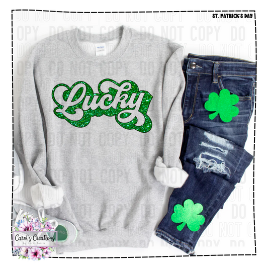 Gray sweatshirt with 'Lucky' in green glitter and denim jeans with green shamrock patches on a white background.