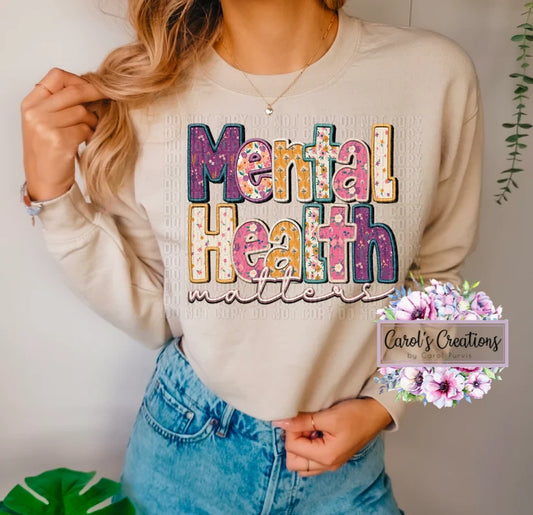 Person wearing a beige sweatshirt with 'Mental Health Matters' text, standing against a neutral background.