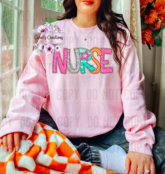 Person wearing a pink 'NURSE' sweatshirt with colorful letters, sitting on a couch.