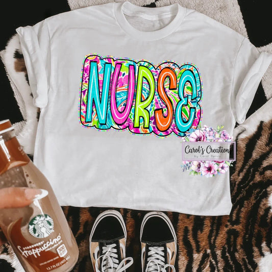 White t-shirt with colorful 'NURSE' design on a patterned surface with a Starbucks cup and sneakers.