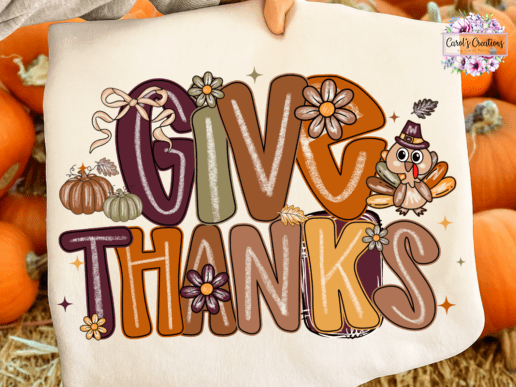 A fabric tote bag held by a hand, featuring a colorful 'GIVE THANKS' autumn graphic with pumpkins, flowers, and a cartoon turkey, set against a background of real pumpkins and straw.