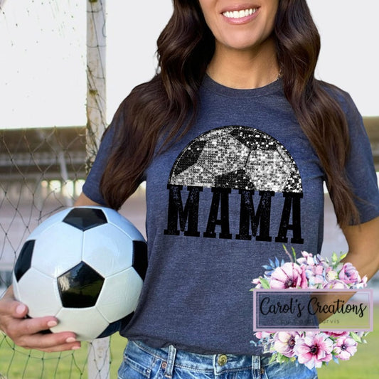 Woman wearing a blue t-shirt with 'MAMA' and a sequin design, holding a soccer ball on a sports field.