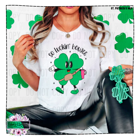 Person wearing a white t-shirt with a green cartoon character and 'So Luckin' Bouge' text, surrounded by shamrock patterns.
