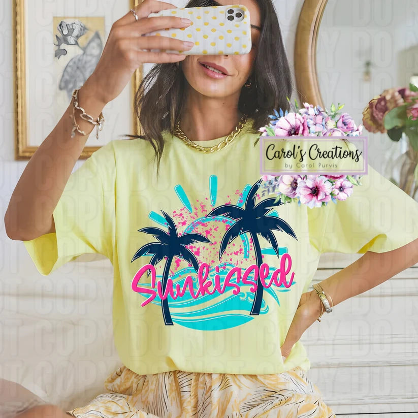 Person wearing a yellow t-shirt with palm tree design and 'Shakies' text, taking a mirror selfie.