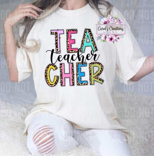 Person wearing a white t-shirt with 'TEACHER' in colorful letters, sitting on a white surface.