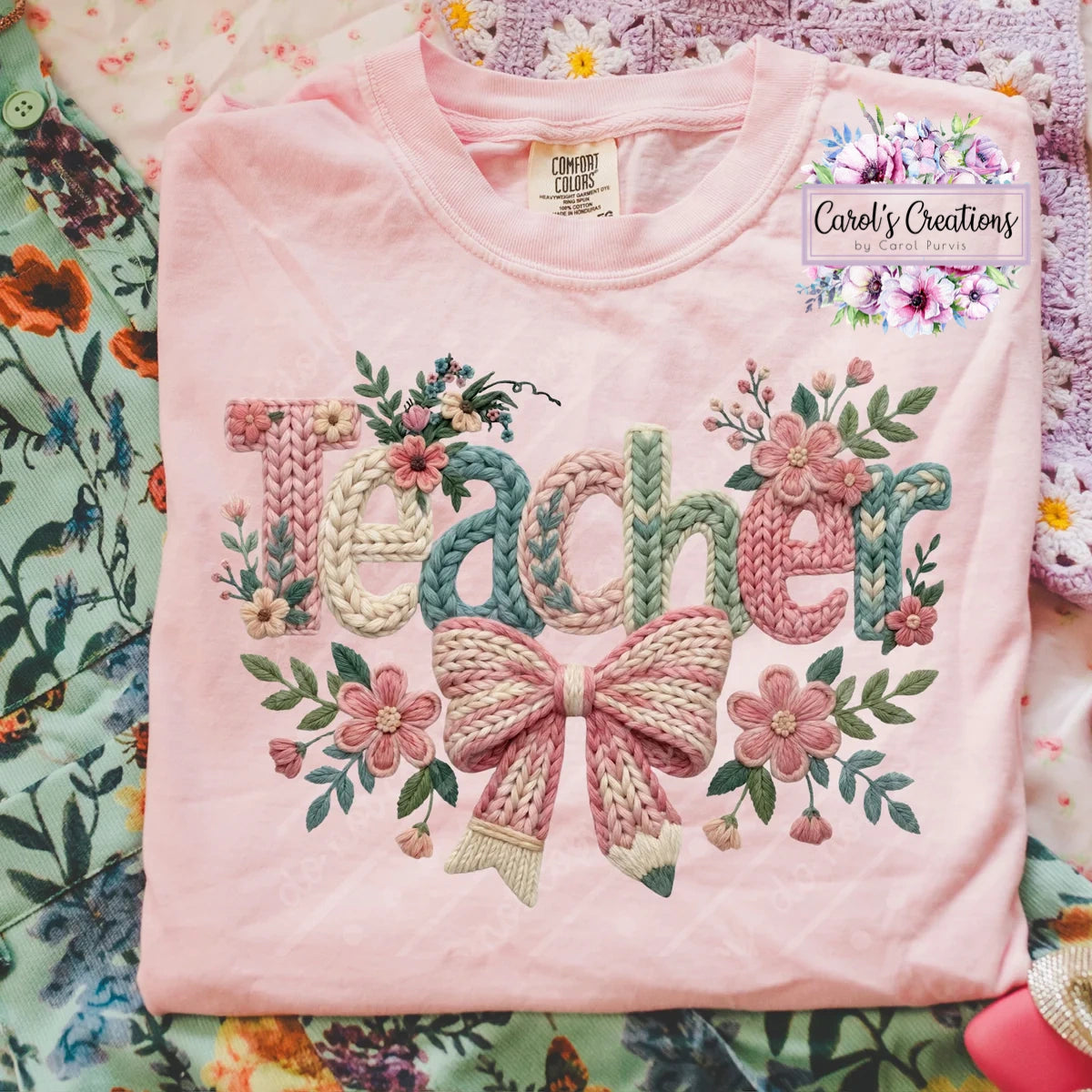 Pink sweatshirt with 'Teacher' and floral embroidery on a colorful fabric background