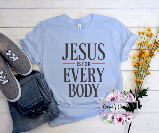 Light blue t-shirt with 'Jesus is for Every Body' text, paired with jeans and slippers on a wooden surface.