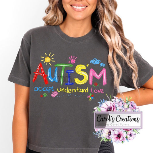 Person wearing a dark gray t-shirt with colorful 'AUTISM' text and supporting phrases, with 'Carol's Creations' branding.