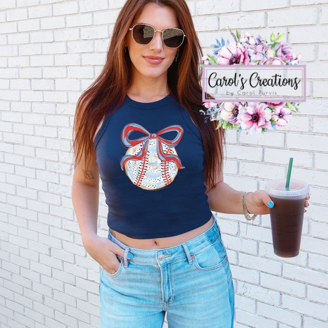 Woman wearing a navy blue crop top with a decorative bow design, holding a drink, against a white brick wall.