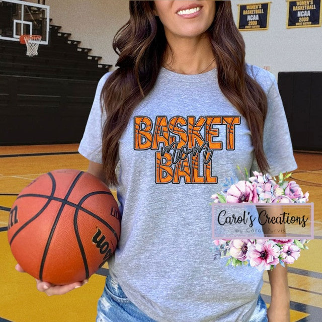 Person wearing a 'Basket Ball' t-shirt holding a basketball on a gymnasium floor.