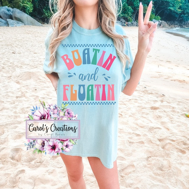 Woman wearing a light blue t-shirt with colorful text on a beach, featuring 'Carol's Creations' logo.