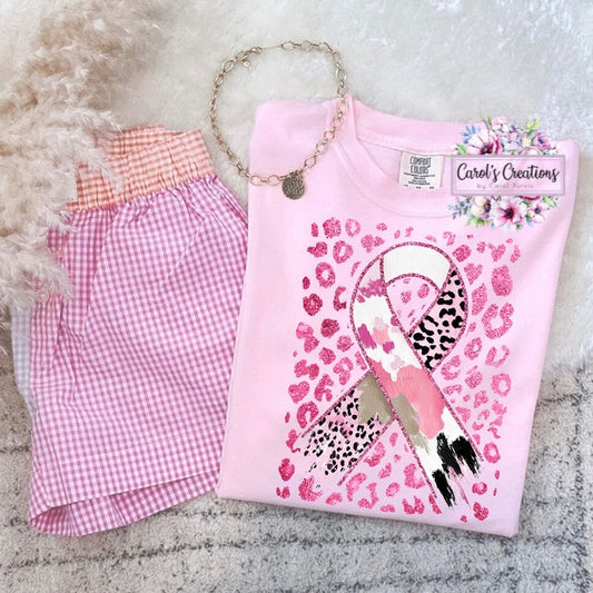 Pink t-shirt with a design, pink shorts, and a necklace on a textured surface.
