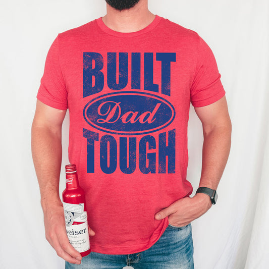 Person wearing a red t-shirt with 'Built Dad Tough' text, holding a bottle.
