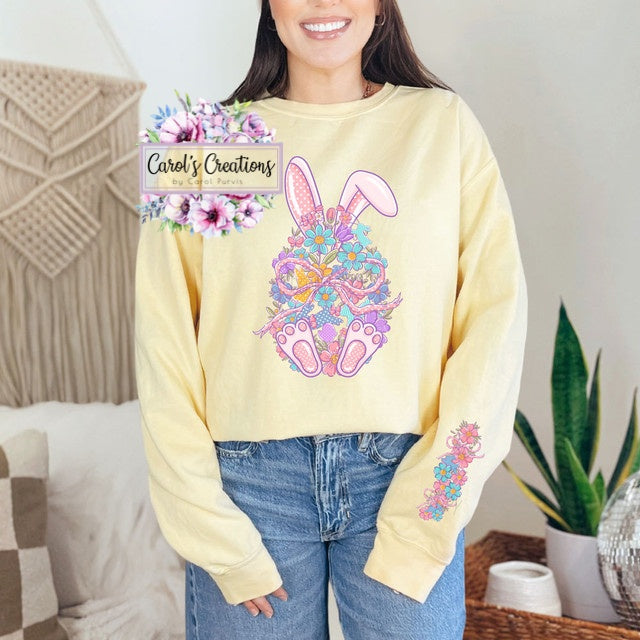 Person wearing a yellow sweatshirt with floral bunny design, standing in a cozy living room.