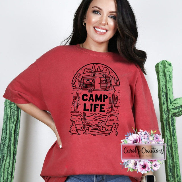 Woman wearing a red 'Camp Life' t-shirt with a desert graphic, standing next to a cactus.