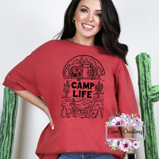 Woman wearing a red 'Camp Life' t-shirt with a desert graphic, standing next to a cactus.