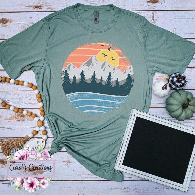 Green t-shirt with a scenic design on a wooden surface with decorative items.